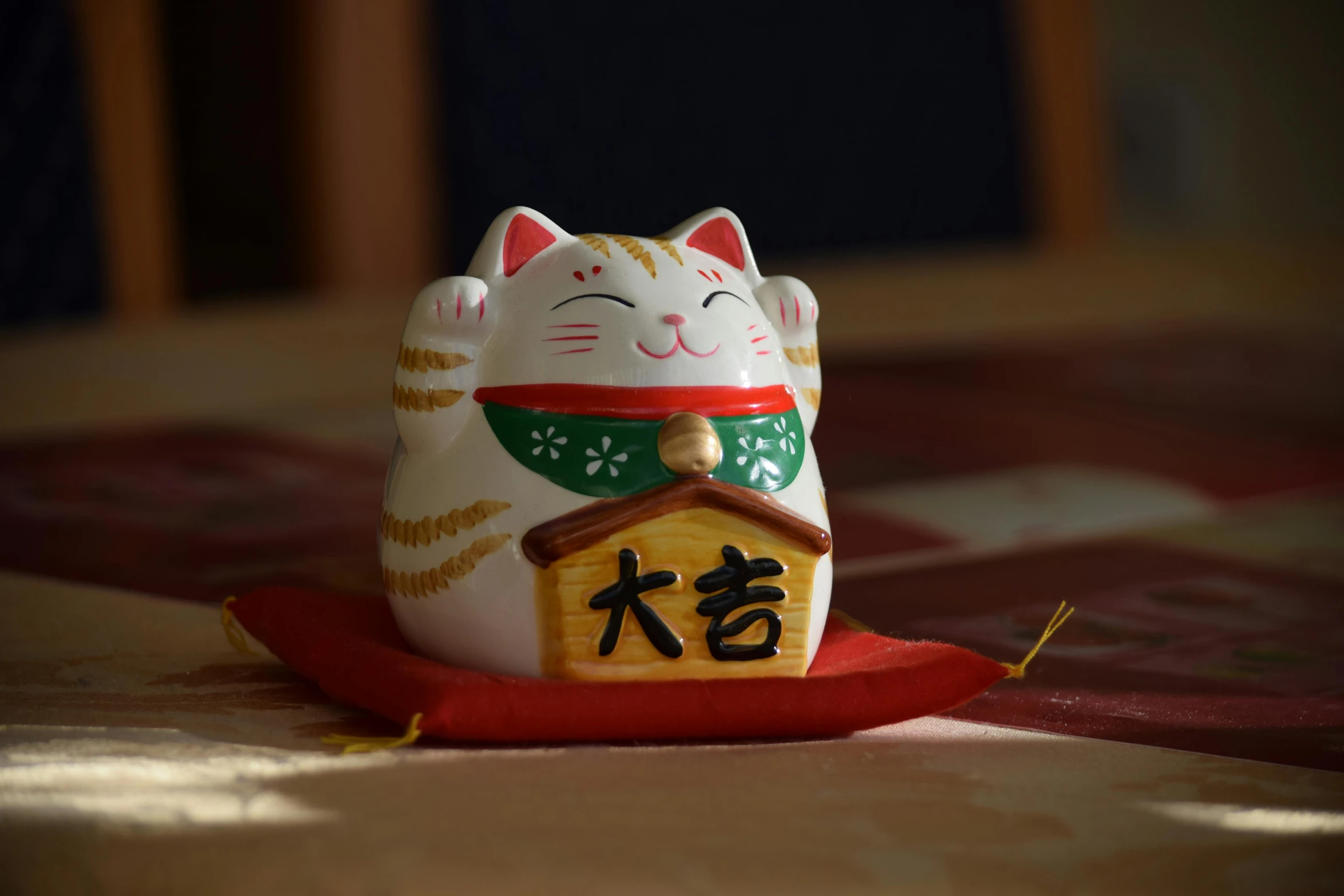 a close up of a cat figurine on a table, a picture, inspired by Miao Fu, unsplash, mingei, holding a golden bell, with white kanji insignias, multi - coloured, japanese house