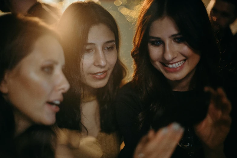 a group of women standing next to each other at a party, a picture, trending on pexels, girl with dark brown hair, background image, warm glow, dark people discussing