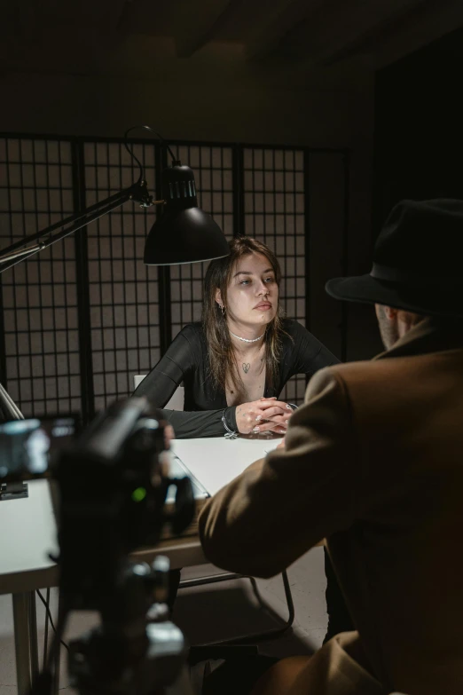 a man and a woman sitting at a table in front of a camera, dark people discussing, female investigator, shot with sony alpha, in the backrooms