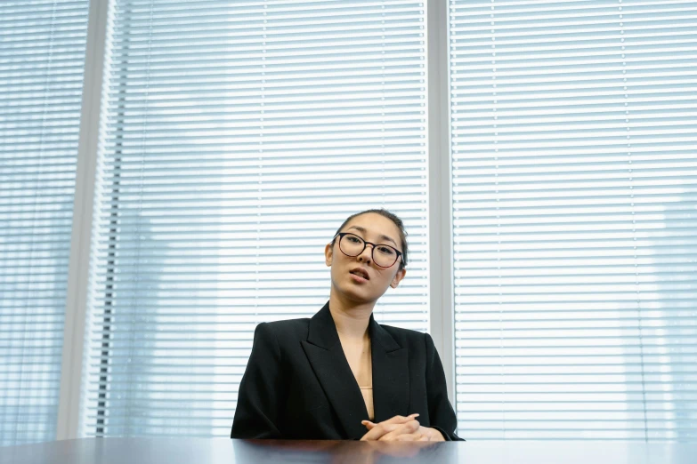 a woman sitting at a table in front of a window, unsplash, shin hanga, wearing a suit and glasses, photographed for reuters, tokujin yoshioka, lawyer