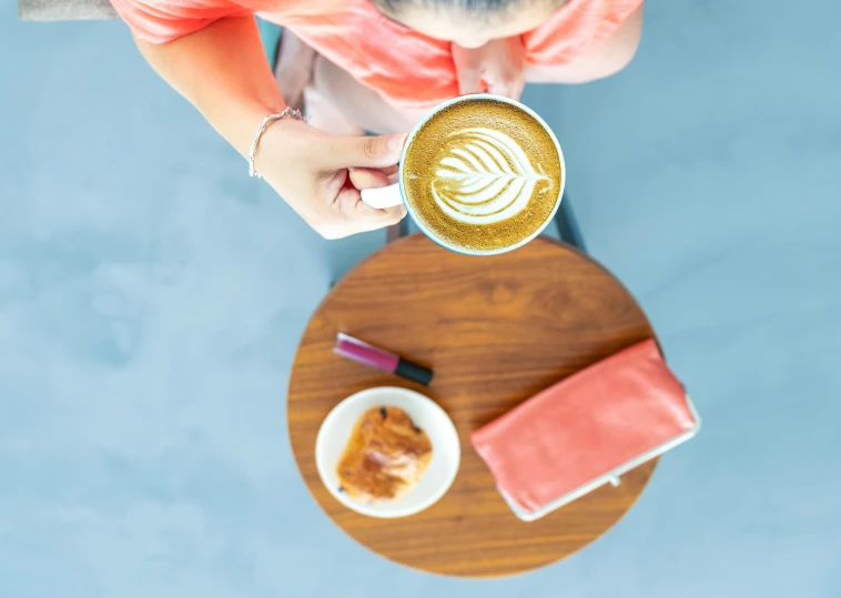 a woman sitting at a table with a cup of coffee, by Carey Morris, trending on unsplash, wide angle shot from above, latte art, vibrant hues, chalk