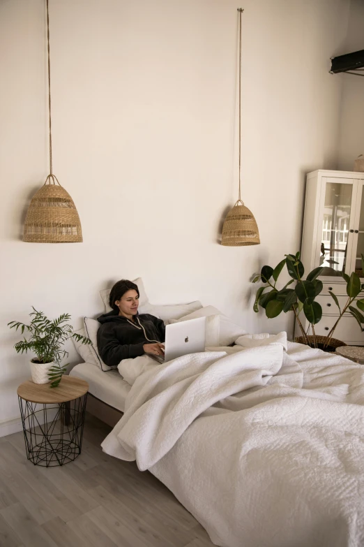 a woman sitting on a bed with a laptop, inspired by Riad Beyrouti, happening, serene bedroom setting, white lighting, asian male, minimalist and clean