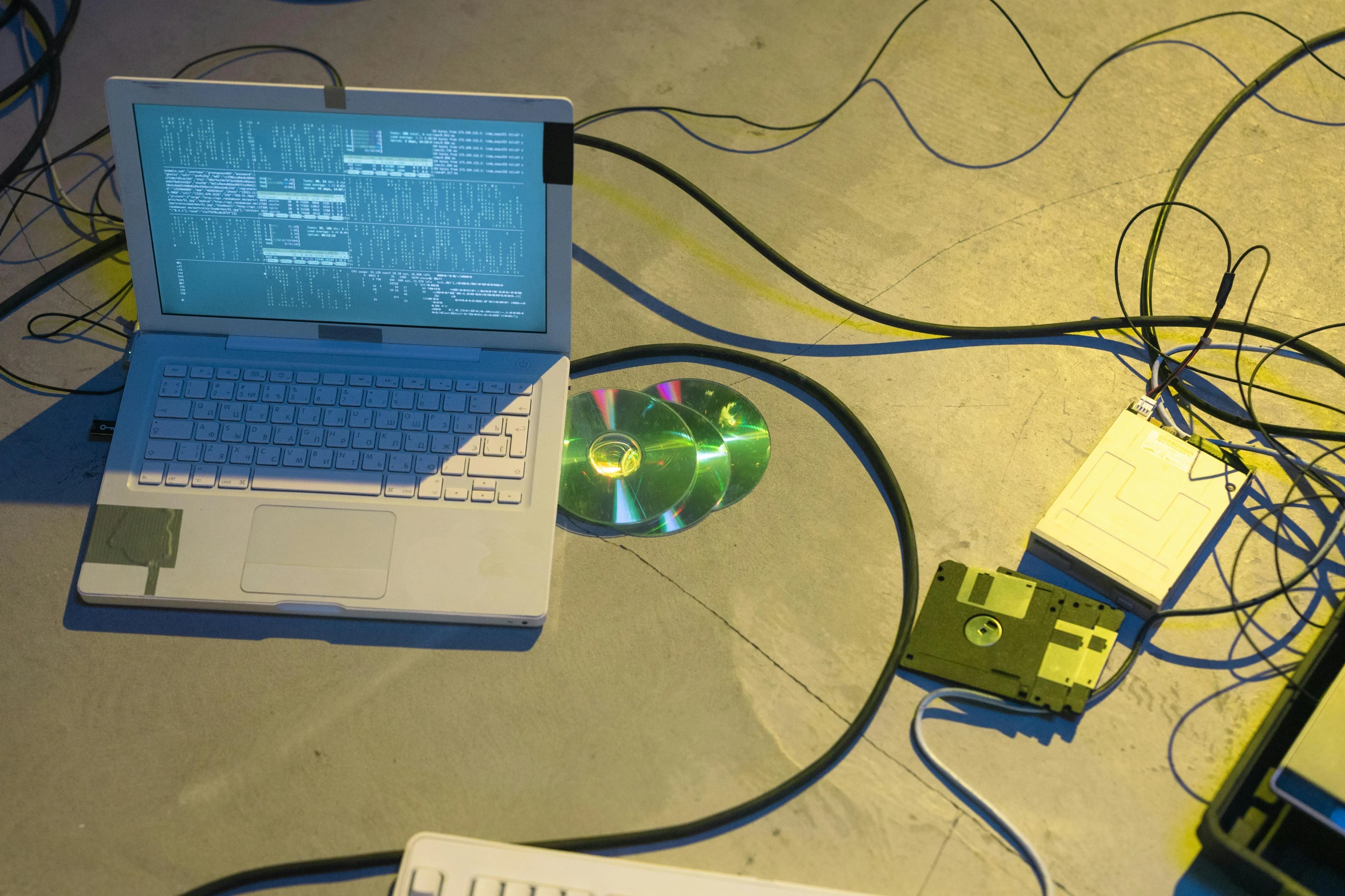 a laptop computer sitting on top of a table, inspired by Johann Kretzschmer, computer art, cables on floor, synth-wave, cds, in a workshop