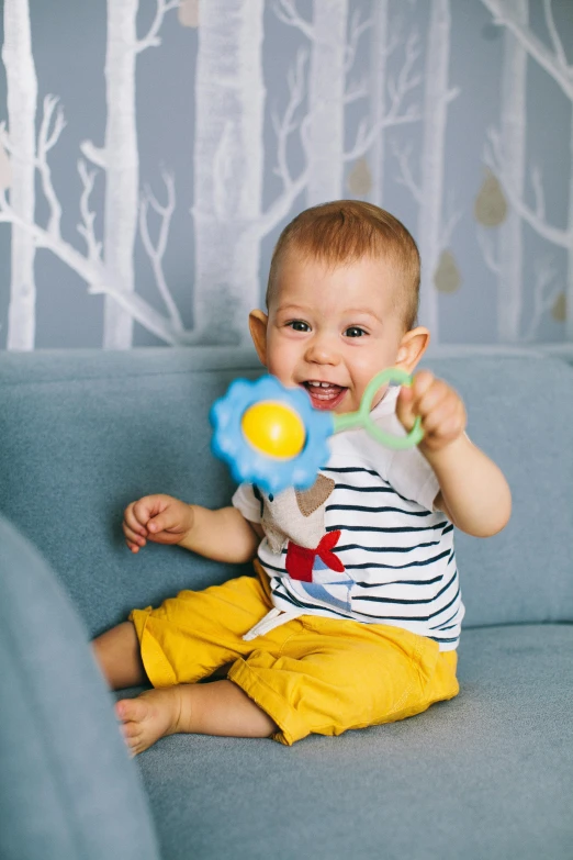 a baby sitting on a couch playing with a toy, inspired by George Barker, holding magic flowers, grey, activity play centre, happy face