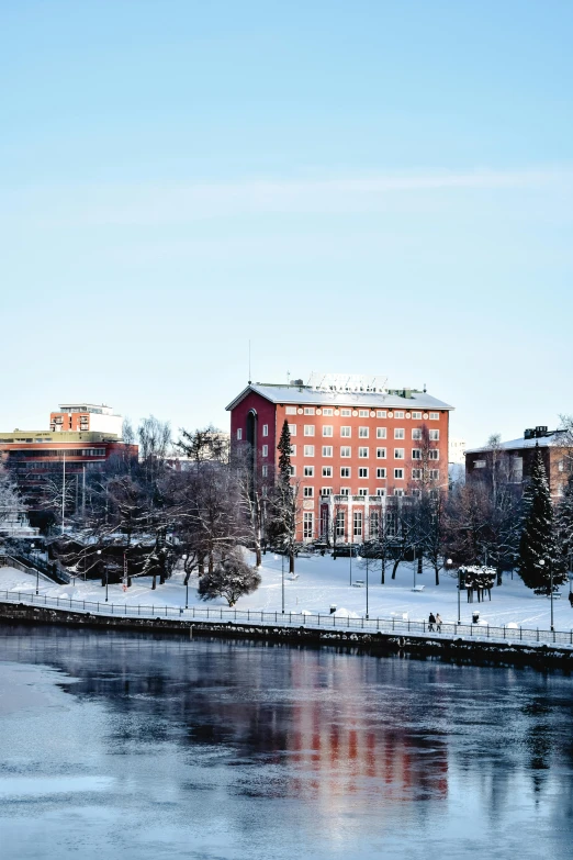 a body of water with buildings in the background, finland, snow, building along a river, college