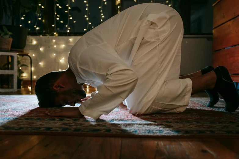 a man is bending over on the floor, hurufiyya, wearing white robe, stomach vibes, lights on, profile image