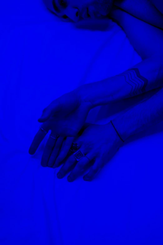 a woman laying on top of a bed under a blue light, an album cover, inspired by Yves Klein, unsplash, symbolism, corrected hands, blacklight aesthetic, laying down with wrists together, low fi