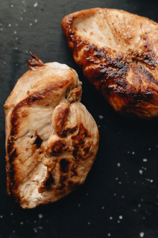 two pieces of chicken sitting on top of a black surface, by Daniel Lieske, unsplash, grilled chicken, plain background, hearts, thumbnail