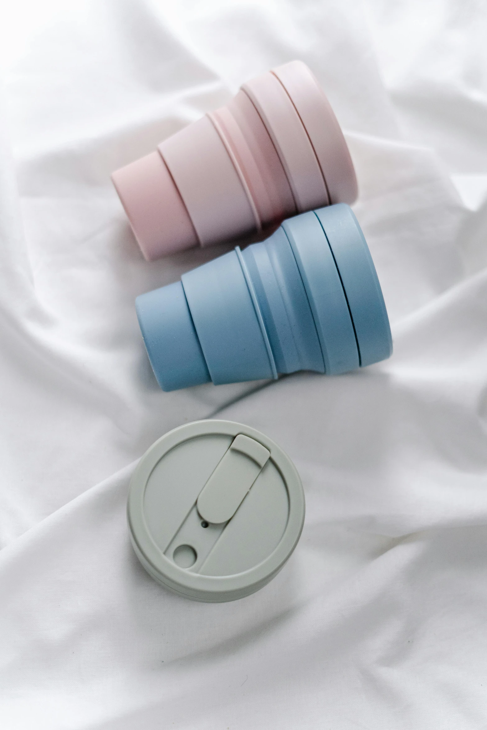 a couple of cups sitting on top of a bed, silicone cover, soft cool colors, folded, promo image