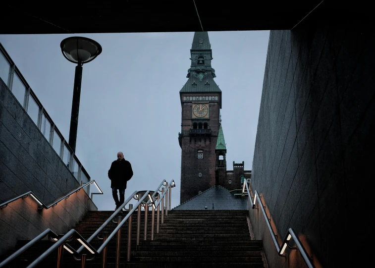 a person walking up a flight of stairs with a clock tower in the background, by Jens Søndergaard, foreboding, helsinki, two towers, portait image