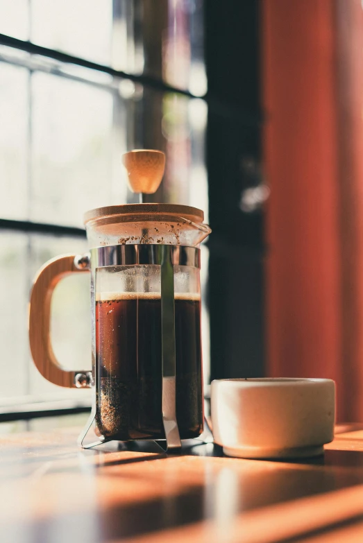 a coffee pot sitting on top of a table next to a cup, by Niko Henrichon, unsplash, square, filled with natural light, a wooden, celebration of coffee products