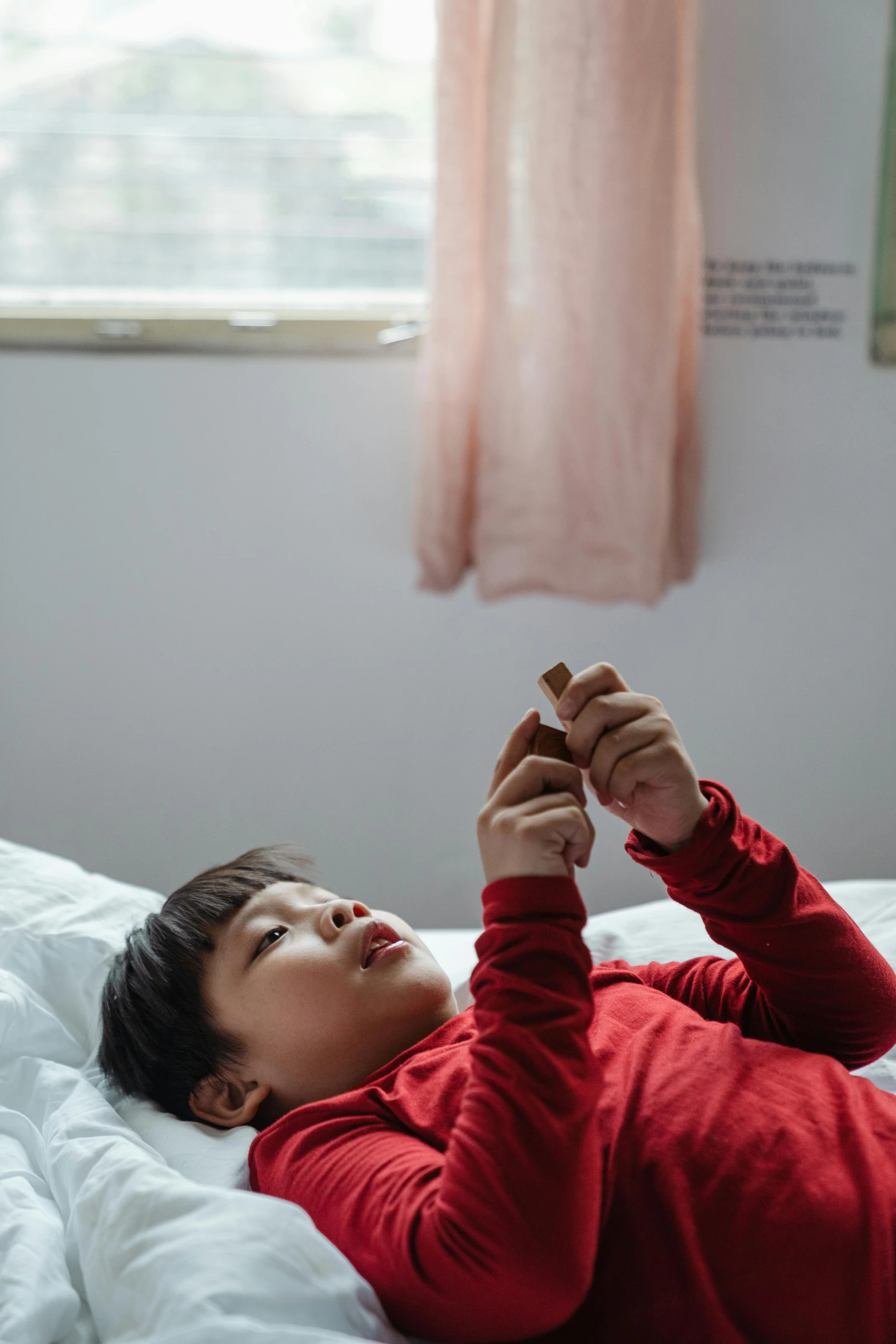 a woman laying on top of a bed next to a window, by Jang Seung-eop, pexels contest winner, kid named finger, he is holding a smartphone, surgery, boy's room