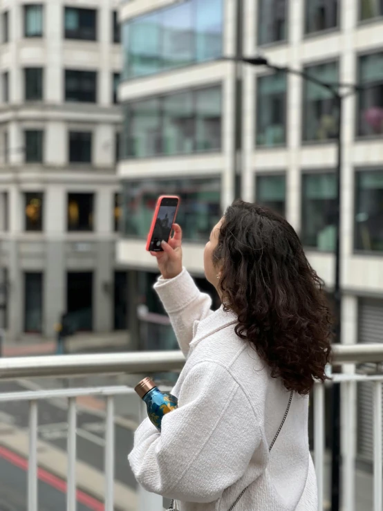 a woman taking a picture on her cell phone, by Carey Morris, pexels contest winner, happening, shot from roofline, holding a bottle, augmented reality, view(full body + zoomed out)