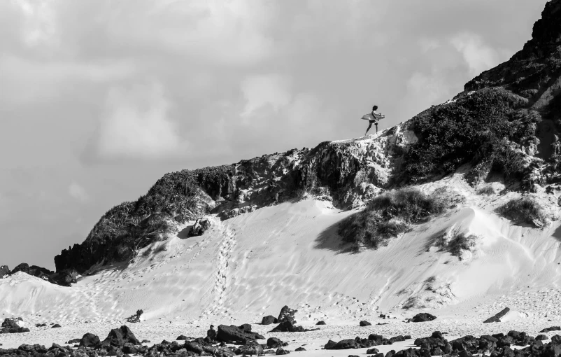 a man standing on top of a snow covered mountain, a black and white photo, unsplash, figuration libre, walking up the sandy beach, surfing, in socotra island, jump