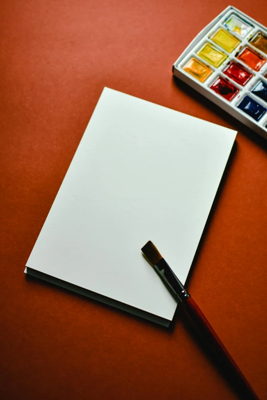 a notepad sitting on top of a table next to a box of watercolors, inspired by Kyffin Williams, pixabay, burnt sienna and venetian red, blank background, card template, multiple stories