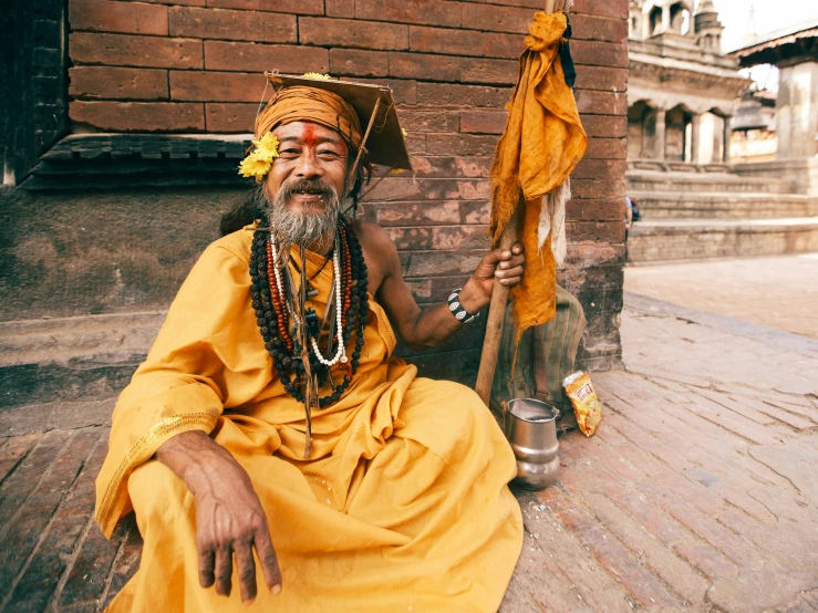 a man sitting on the steps of a building, a photo, pexels contest winner, renaissance, wise old indian guru, orange and yellow costume, wearing dirty travelling clothes, dressed as an oracle