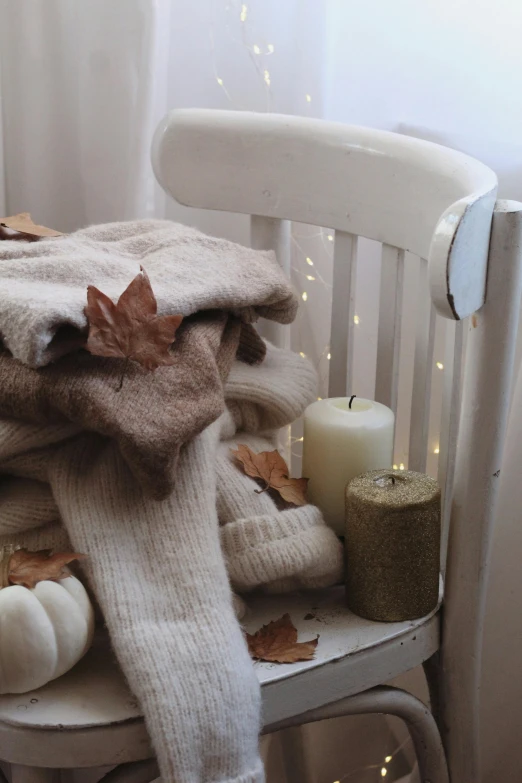 a pile of blankets sitting on top of a chair, a still life, by Aileen Eagleton, pexels, autumn leaves falling, white candles, cream and white color scheme, mittens