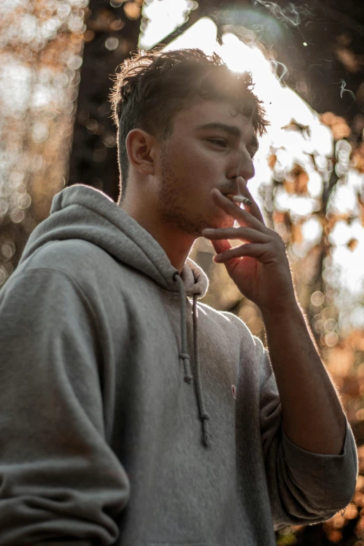 a young man smokes a cigarette in the woods, trending on pexels, wearing a grey hooded sweatshirt, lean man with light tan skin, #oc, profile pic