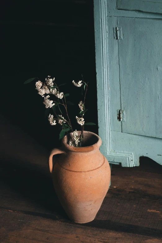 a vase with flowers in it sitting on a wooden floor, inspired by Elsa Bleda, trending on unsplash, faded chipped paint, wooden cabinet, almond blossom, terracotta