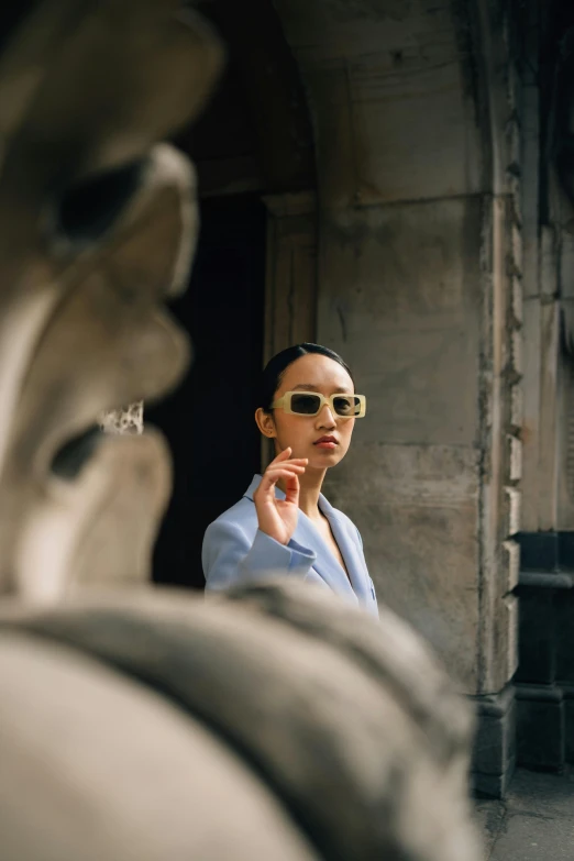 a woman wearing sunglasses standing in front of a building, by Nina Hamnett, trending on unsplash, visual art, li bingbing, stone and glass and gold, pointing at the camera, sophisticated