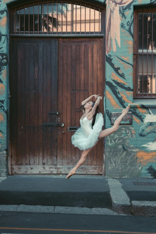 a woman jumping in the air in front of a building, a picture, by Elizabeth Polunin, pexels contest winner, arabesque, portrait of a ballerina, australia, door, 15081959 21121991 01012000 4k