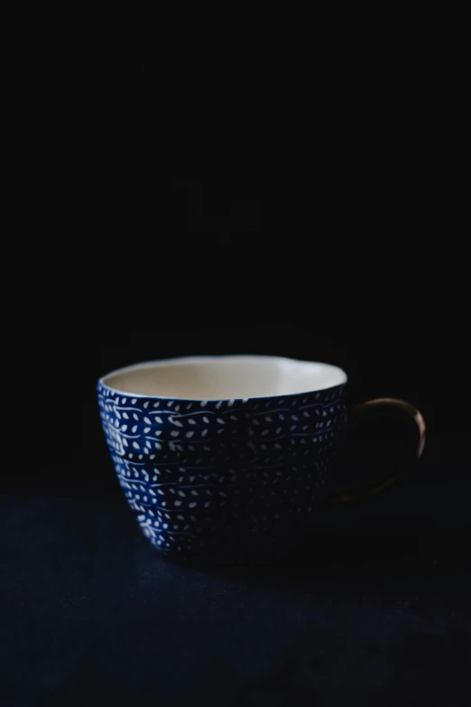 a coffee cup sitting on top of a table, by Jessie Algie, unsplash, folk art, dark blue, subtle pattern, made of glazed, three - quarter view