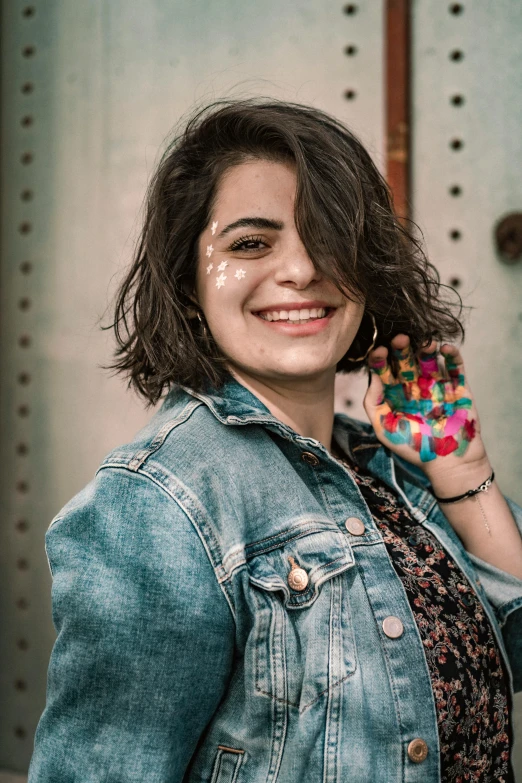 a woman with painted hands posing for a picture, by Lucia Peka, pexels contest winner, jean jacket, dark short curly hair smiling, pale-skinned persian girl, ( ( ( colorful ) ) )