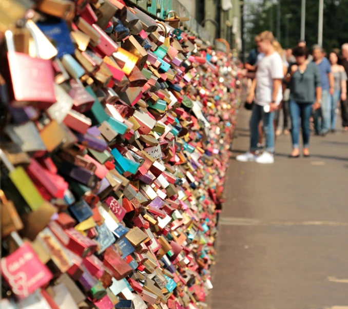 a group of people standing next to a wall covered in padlocks, a picture, bridge, romantic lead, instagram post, 15081959 21121991 01012000 4k