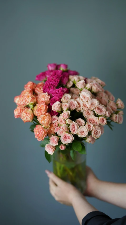 a close up of a person holding a vase of flowers, inspired by Pierre-Joseph Redouté, unsplash, crown of peach roses, pink and orange, detailed wide shot, various sizes