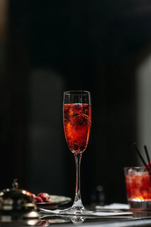 a close up of a glass of wine on a table, inspired by Jacopo Bellini, red sprites in the atmosphere, bubbly, vibrant dark mood, cocktail bar