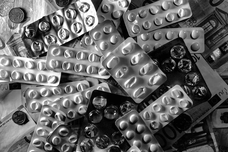 a bunch of pills sitting on top of a pile of money, a black and white photo, by Jan Rustem, plasticien, palettes, metallic buttons, shot with iphone 1 0, abstract photography