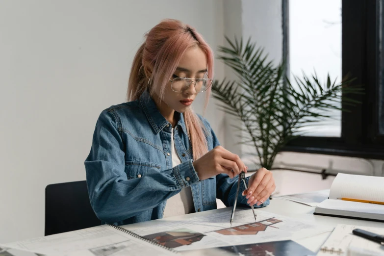 a woman sitting at a table cutting a piece of paper, trending on pexels, hyperrealism, wearing denim, wearing square glasses, professional photo, elaborate illustration