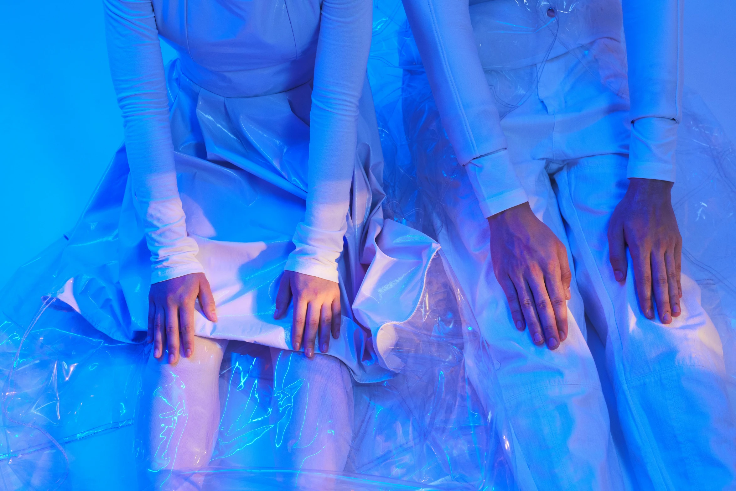 a couple of women sitting next to each other, an album cover, by Julia Pishtar, unsplash, process art, blue shiny lighting, white gloves, futuristic fashion show, plastic and fabric