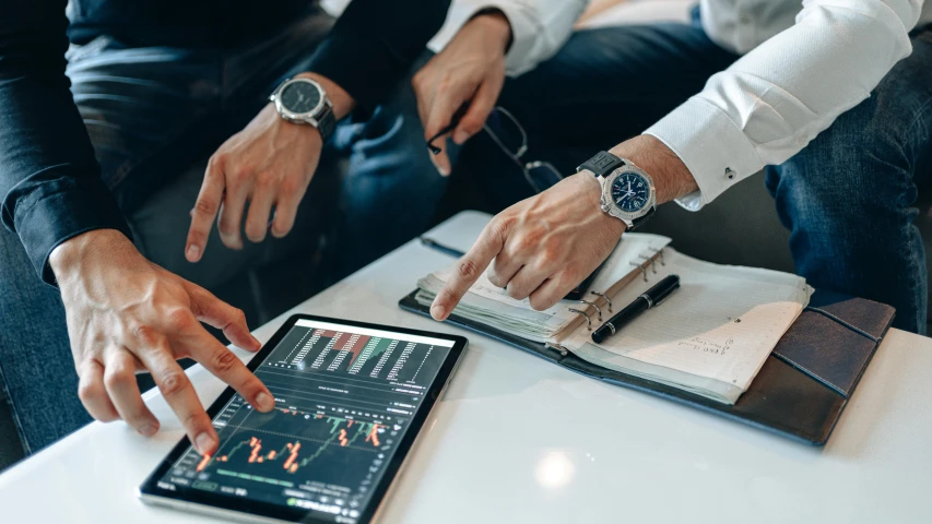 a couple of men sitting next to each other on top of a table, trending on pexels, analytical art, displaying stock charts, handheld, lachlan bailey, low quality photo