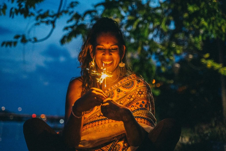 a woman sitting on the ground holding a sparkler, indian girl with brown skin, making the best smug smile, profile image, hindu stages of meditation