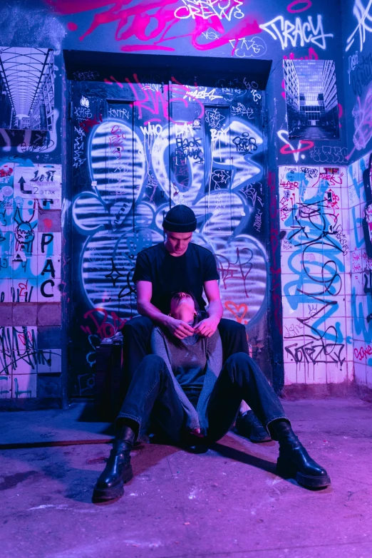 a man sitting in front of a building covered in graffiti, purple scene lighting, two buddies sitting in a room, bisexual lighting, embracing