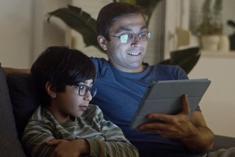 a man sitting next to a little boy on a couch, computer art, wearing medium - sized glasses, night setting, took on ipad, still image from tv series