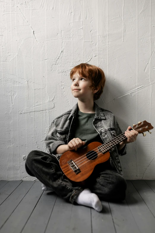 a young boy sitting on the floor playing a guitar, an album cover, by James Warhola, pexels contest winner, ginger hair with freckles, ukulele, sittin, studio kai