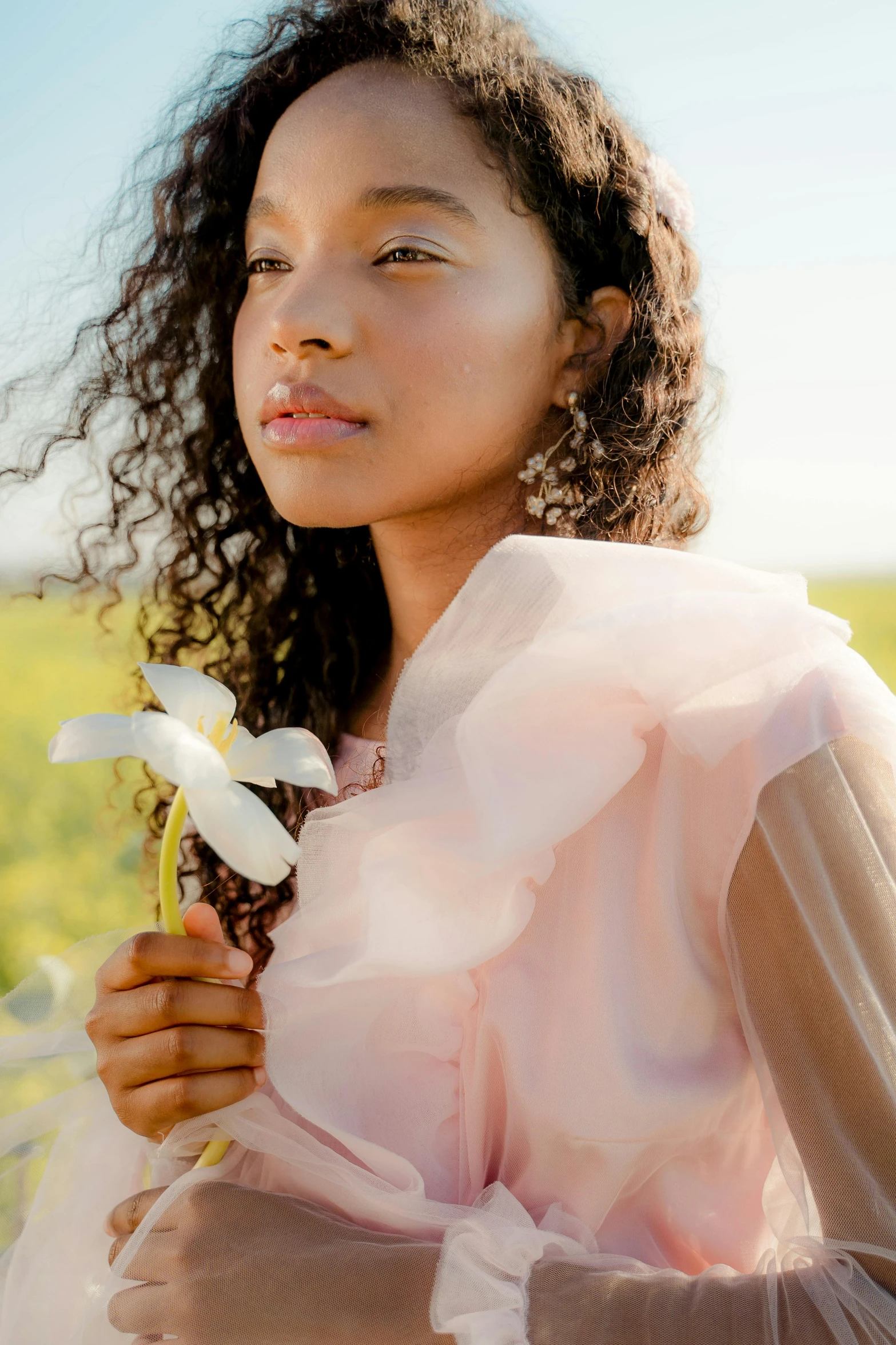 a woman standing in a field holding a flower, trending on pexels, renaissance, wearing organza gown, natural complexion, light pink, dynamic closeup