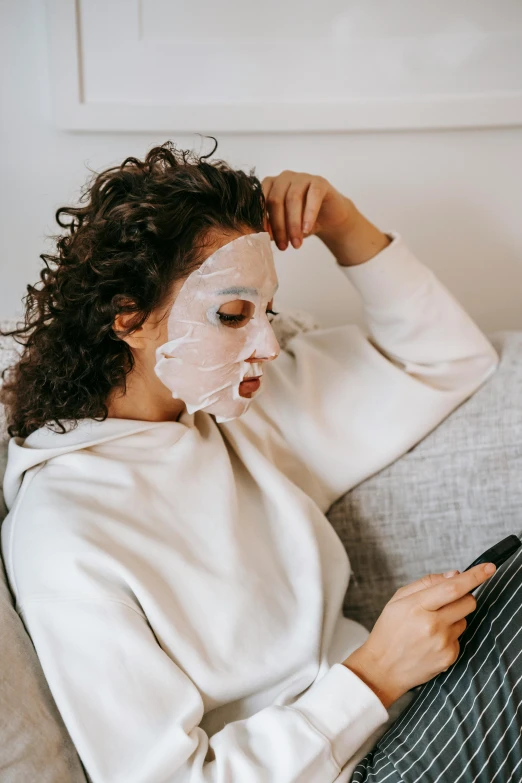 a woman sitting on a couch using a cell phone, a cartoon, trending on pexels, happening, face mask, white powder makeup, wearing white pajamas, pouty face