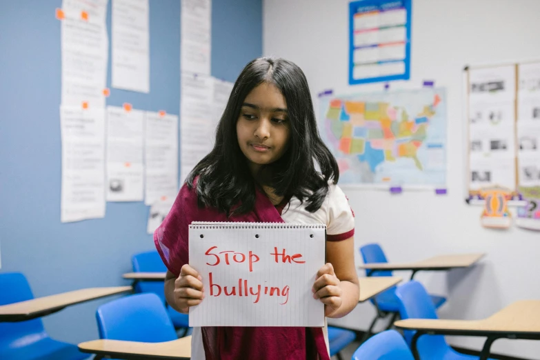 a girl holding a sign that says stop the bullying, trending on unsplash, standing in class, hindu, getty images, ameera al-taweel