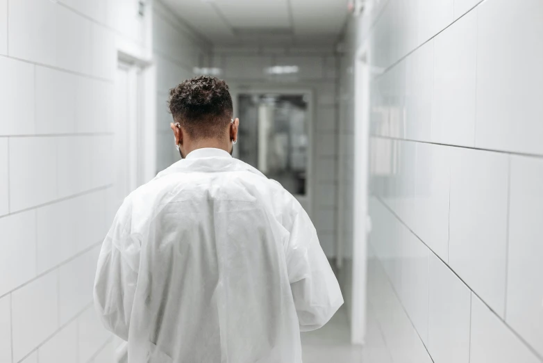 a man in a white lab coat standing in a hallway, pexels contest winner, happening, from back, healthcare worker, non-binary, operating room