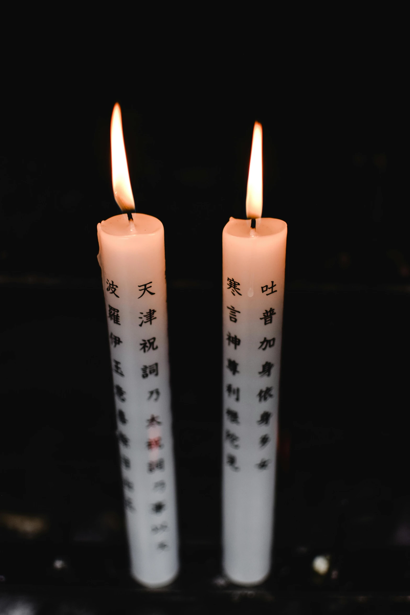 two white candles sitting next to each other on a table, sōsaku hanga, kanji, on a black background, square, taiwan