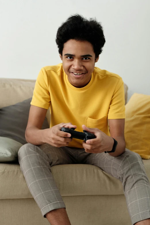 a man sitting on a couch holding a video game controller, wearing a modern yellow tshirt, black teenage boy, promo image, lean man with light tan skin