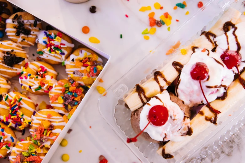 a banana split sitting on top of a table next to a box of donuts, by Julia Pishtar, pexels, candy land, tie-dye, group photo, white