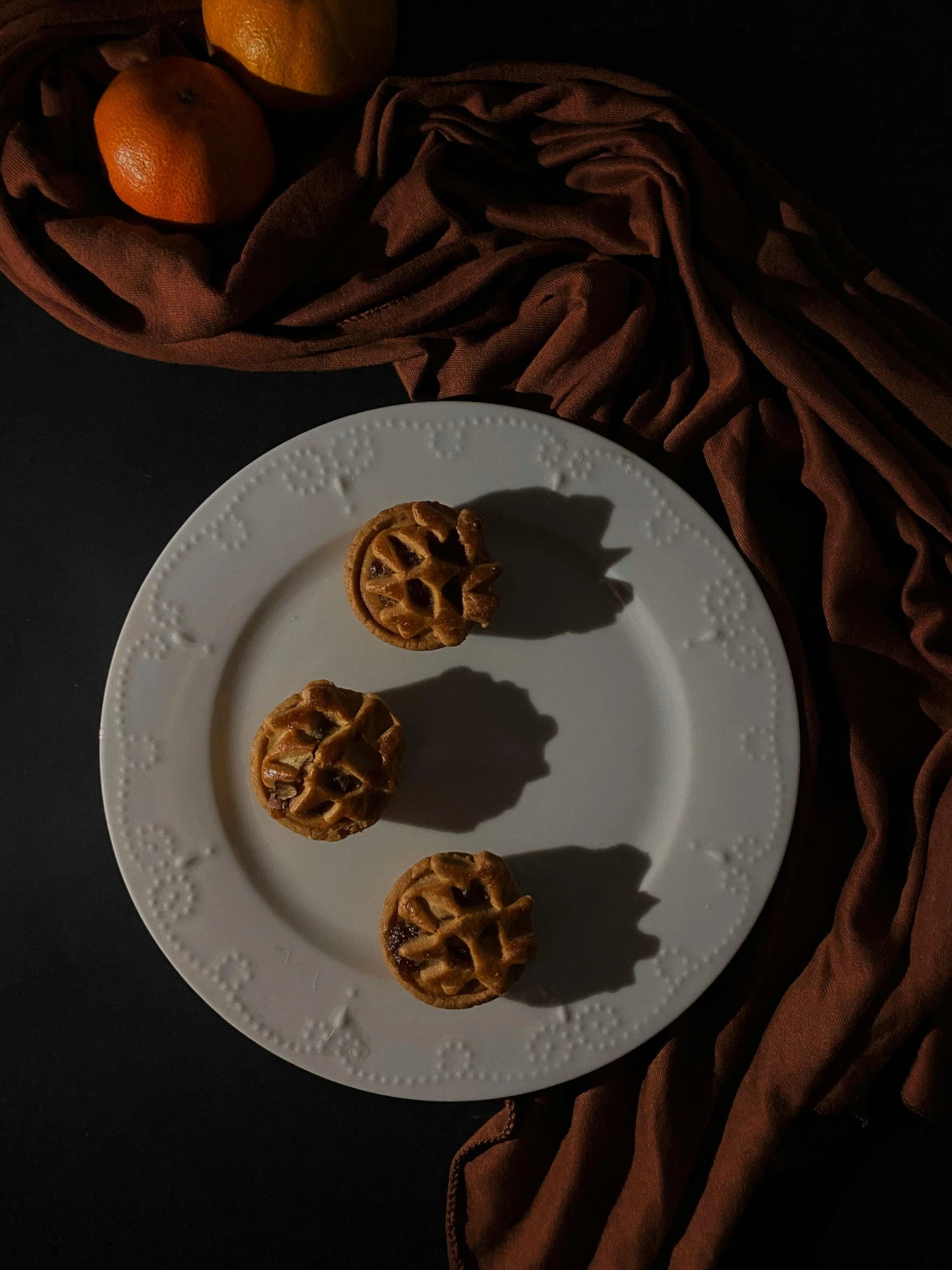 a white plate topped with pretzels next to oranges, a still life, inspired by Théodore Géricault, unsplash, 3 - piece, apple pie, dark tone, pumpkins