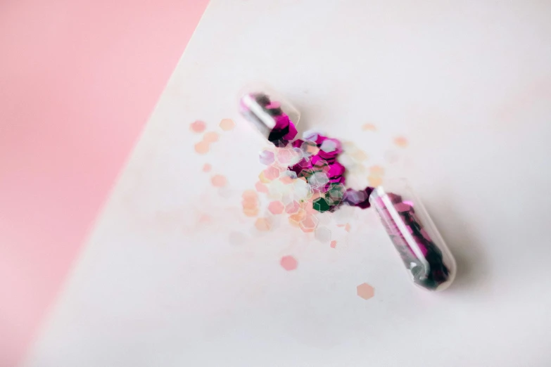 a couple of pills sitting on top of a table, a microscopic photo, by Emma Andijewska, trending on pexels, confetti, pen on white paper, pink diamonds, abstract design