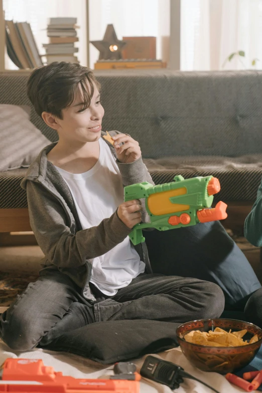 a couple of people that are sitting on the floor, next to it is a toy ray gun, kid playing with slime monster, promo image, snacks