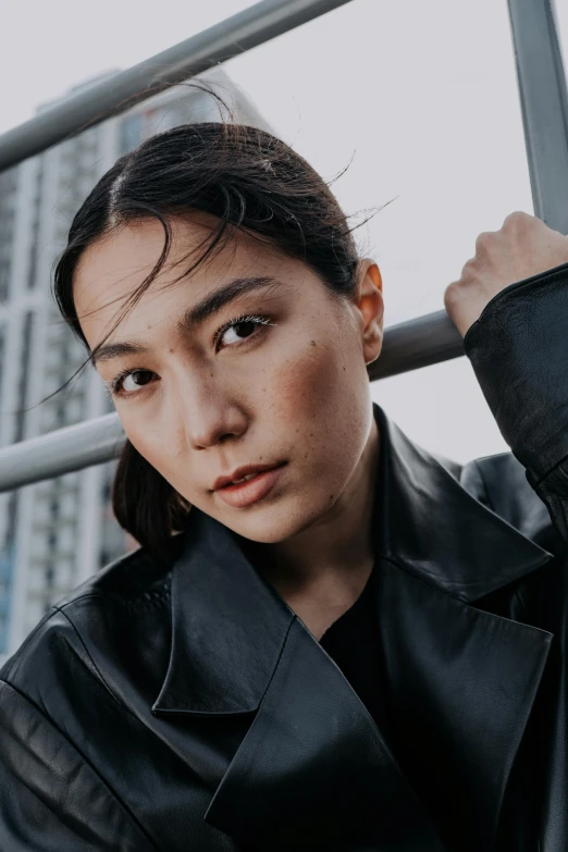 a woman in a black jacket leaning against a railing, inspired by Ruth Jên, trending on pexels, asian face, wearing leather, a portrait of issey miyake, hybrid of gal gadot