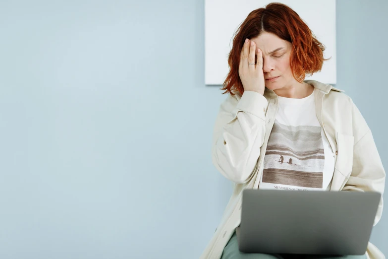 a woman sitting in front of a laptop computer, a picture, by Julia Pishtar, trending on pexels, sad christina hendricks, on a pale background, over it's head, nursing